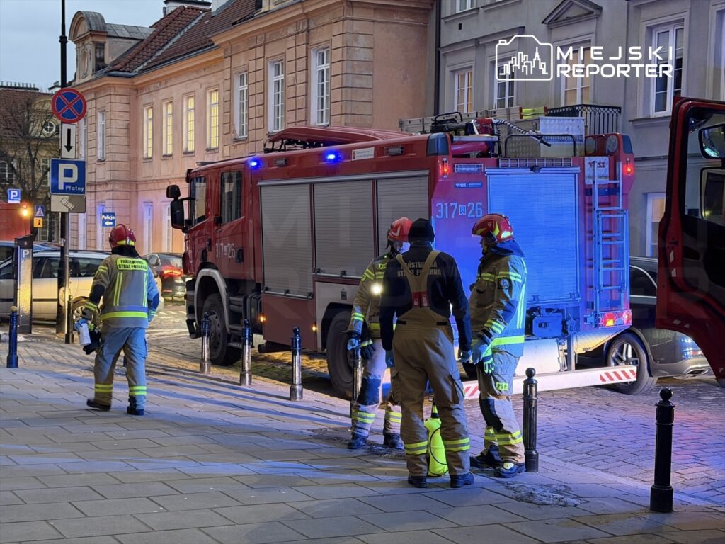 Czterech strażaków w mundurach omawia sytuację obok wozu strażackiego na oświetlonej ulicy.