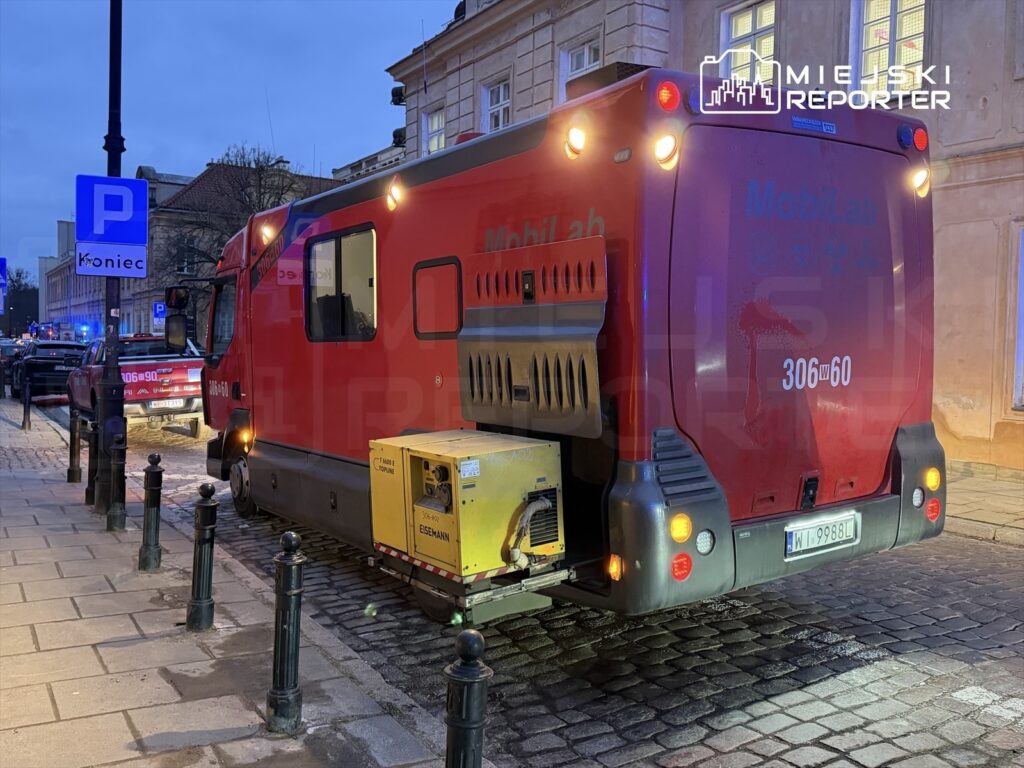 Czerwony pojazd specjalistyczny zaparkowany na wąskiej ulicy, obok znaku parkingowym "Koniec".