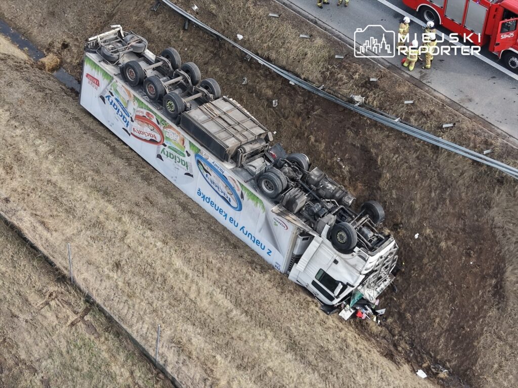 Przewrócony ciężarówka na poboczu drogi, otoczona przez służby ratunkowe.