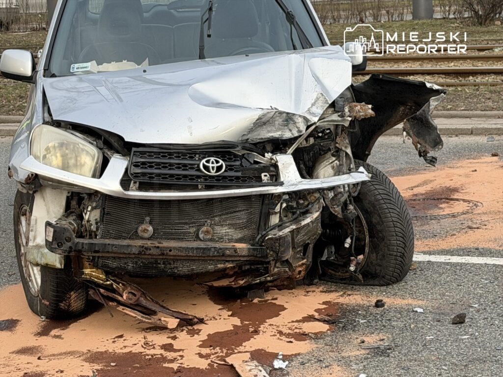 Uszkodzony samochód osobowy marki Toyota z wgniecionym przodem stoi na drodze, obok rozlane płyny eksploatacyjne.