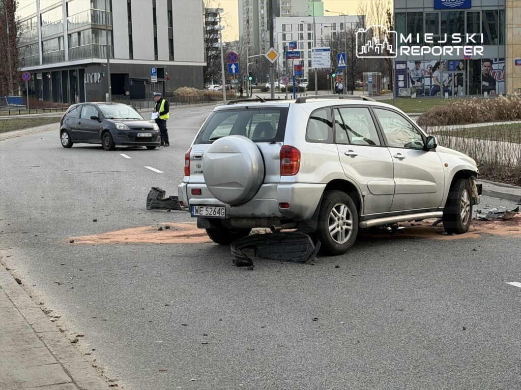 Na drodze stoi uszkodzony samochód osobowy, a obok policyjny funkcjonariusz spisuje informacje.