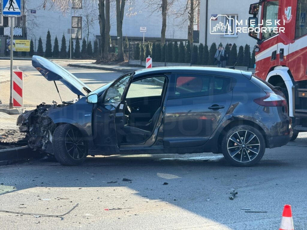 Uszkodzony samochód osobowy z otwartą maską stoi na skrzyżowaniu, obok widać woz strażacki.