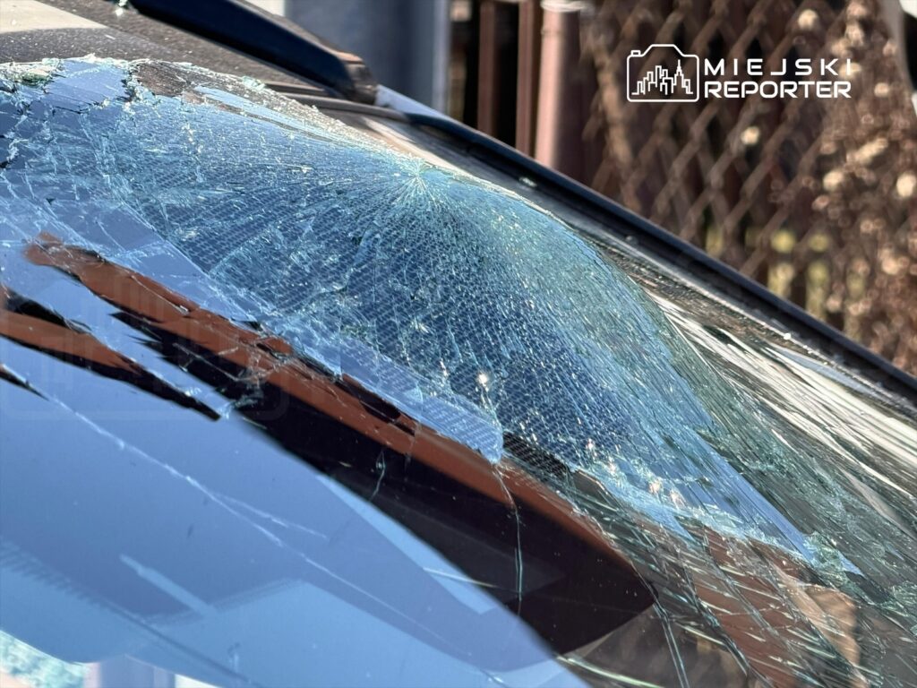 Pęknięta szyba samochodowa z wyraźnymi uszkodzeniami, leżąca na parkingu w słoneczny dzień.