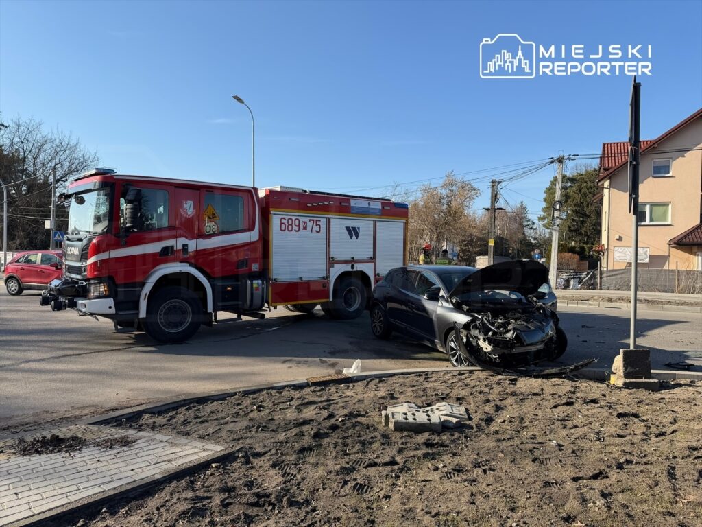 Wóz strażacki zatrzymany obok uszkodzonego samochodu osobowego na skrzyżowaniu w słoneczny dzień.