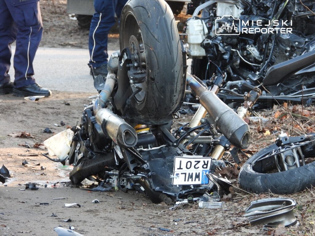 Zniszczony motocykl leży na poboczu drogi, otoczony odłamkami i liśćmi, obok stoją policjanci w mundurach.