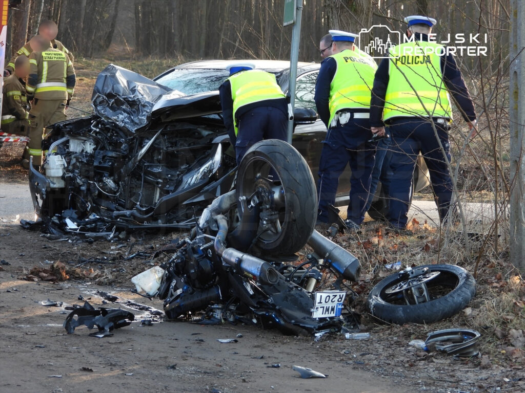 W miejscu wypadku drogowego, policjanci zabezpieczają uszkodzony samochód oraz rozbite elementy motocykla.
