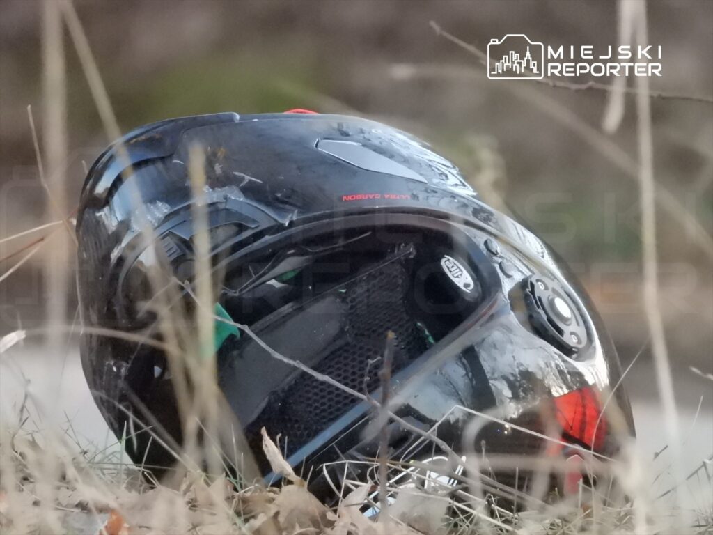 Czarny kask motocyklowy leży na trawie w otoczeniu suchych gałęzi i liści.