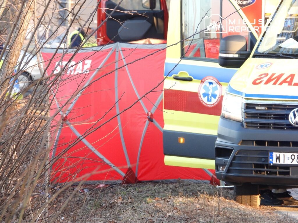 Ratownicy medyczni pracują przy czerwonym namiocie w pobliżu karetki na terenie zdarzenia.