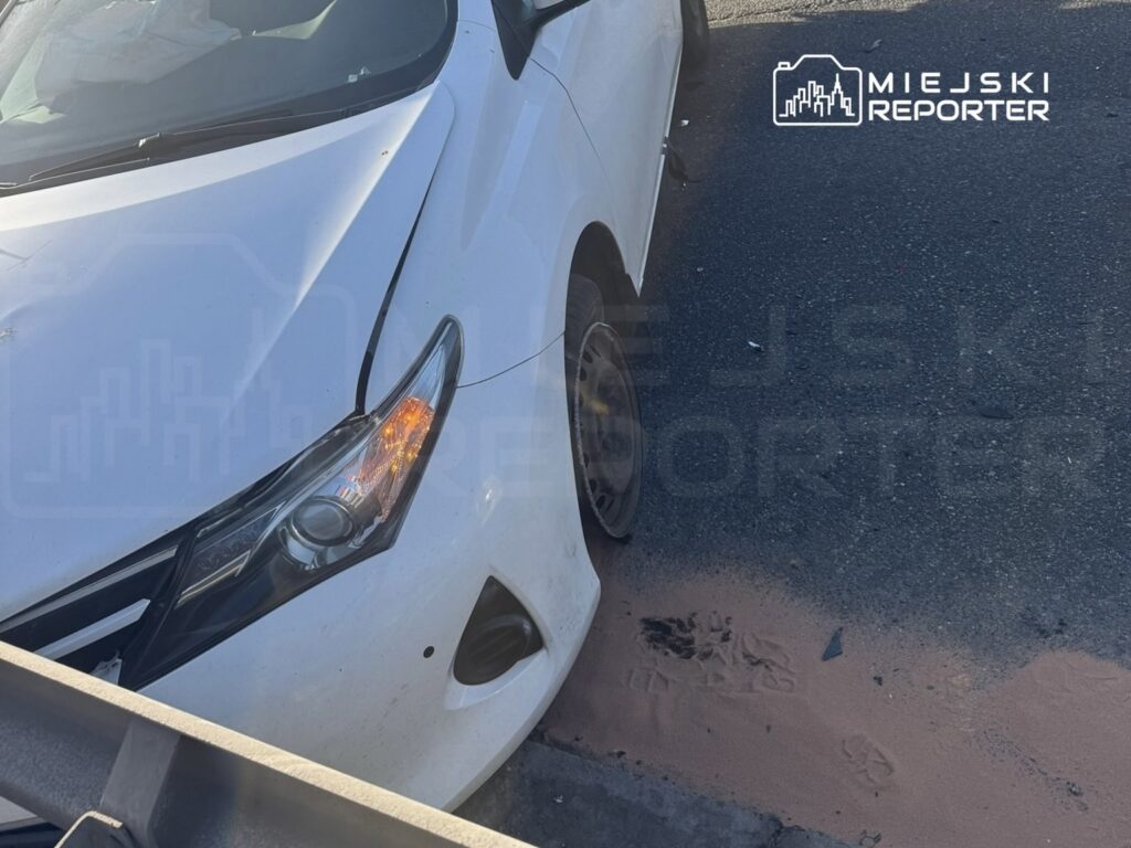Biały samochód osobowy z uszkodzoną przednią częścią zaparkowany na drodze, obok widoczne ślady na asfalcie.