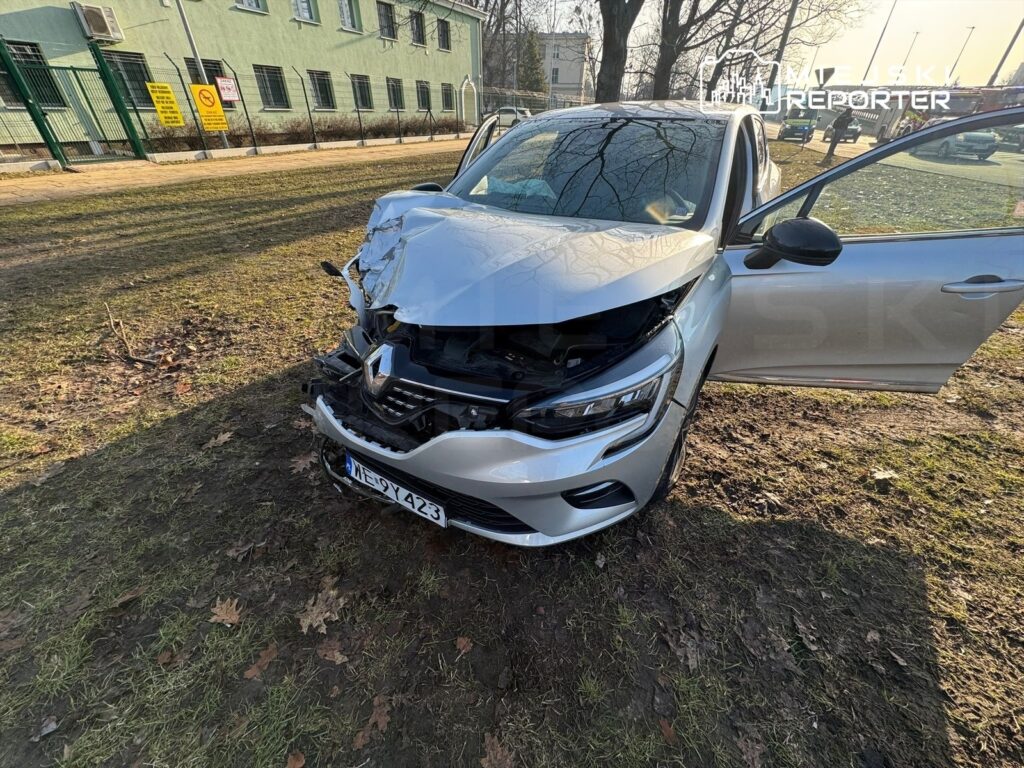 Uszkodzony samochód osobowy marki Renault z wgniecioną maską stoi na trawie obok budynku.