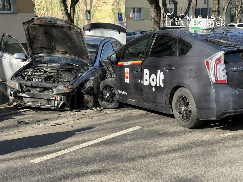Zderzenie dwóch samochodów na ulicy, jeden z pojazdów z uszkodzoną maską i wgniecionym przodem.