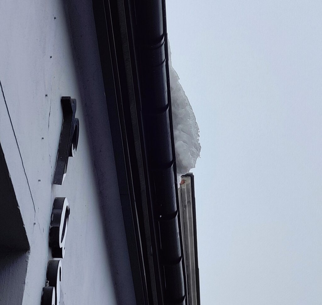 Sople lodu zwisające z rynny budynku pod szarym niebem.
