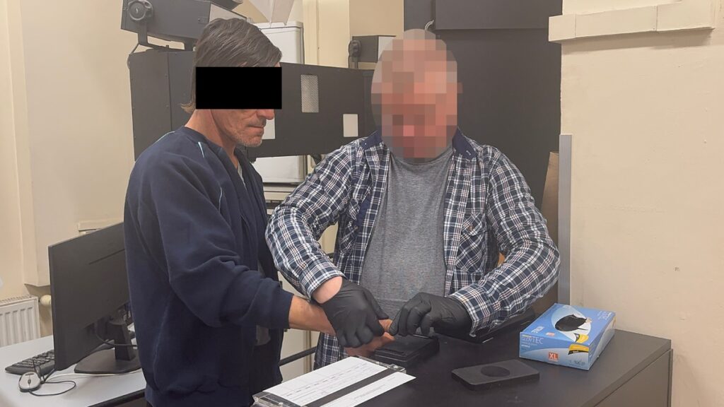 Mężczyzna w ciemnym ubraniu pomaga innemu mężczyźnie w zakładaniu rękawiczek na stacji roboczej.