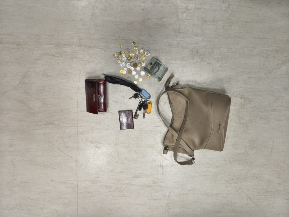 Beżowa torebka leży na jasnej powierzchni obok portfela, kluczy, monet i banknotów.