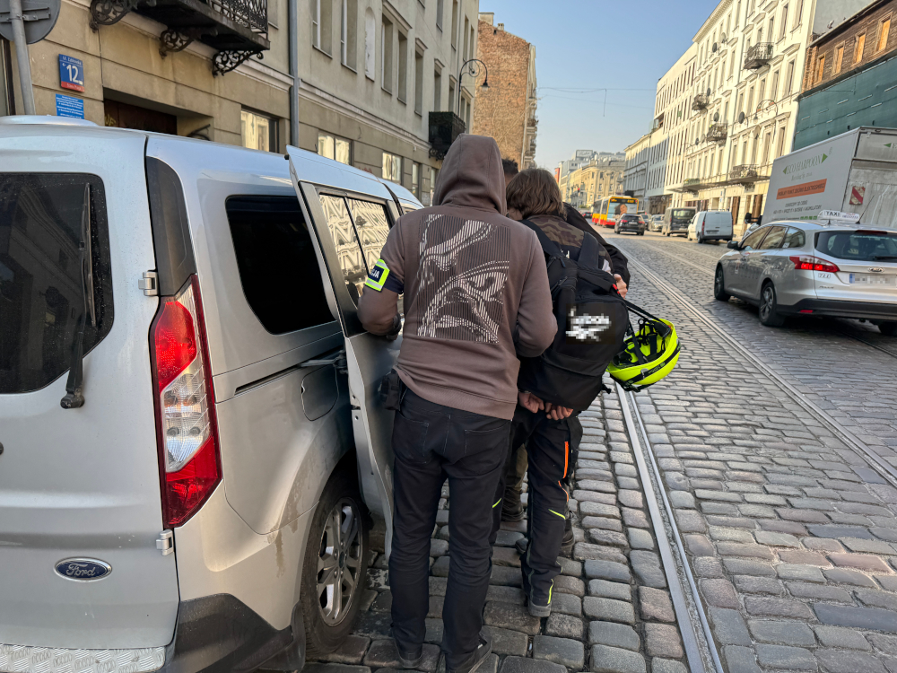 Dwaj mężczyźni w odzieży roboczej sprawdzają wnętrze szarego vana na ulicy z kostki brukowej.