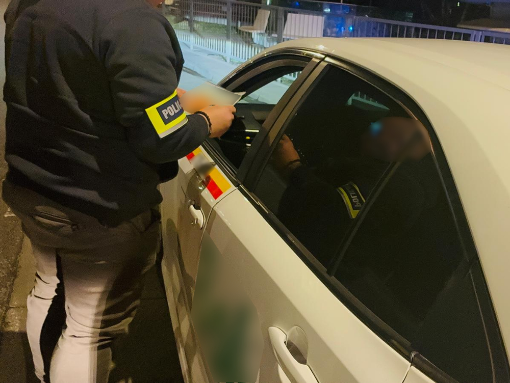 Policjant w mundurze sprawdzający dokumenty kierowcy w białym samochodzie na nocnej ulicy.