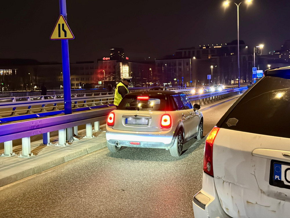Policjant w odblaskowej kamizelce kontrolujący samochód na oświetlonej drodze nocą.