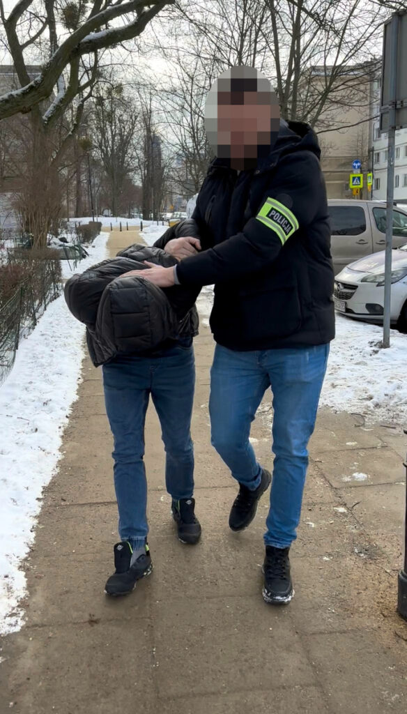 Funkcjonariusz policji w mundurze zatrzymuje mężczyznę na chodniku w zimowej scenerii.