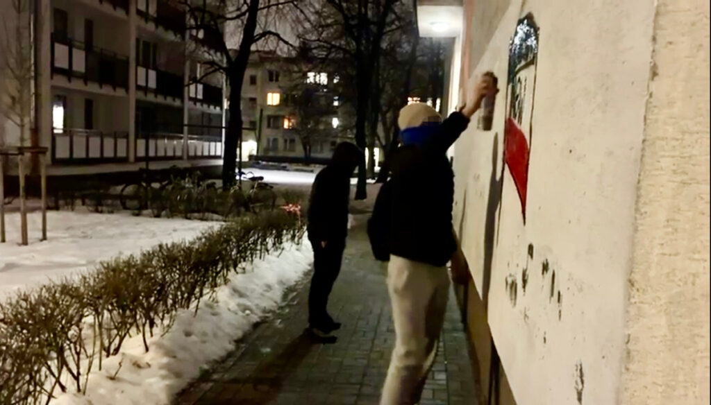 Dwaj mężczyźni malują graffiti na ścianie budynku w nocy, obok leży śnieg.