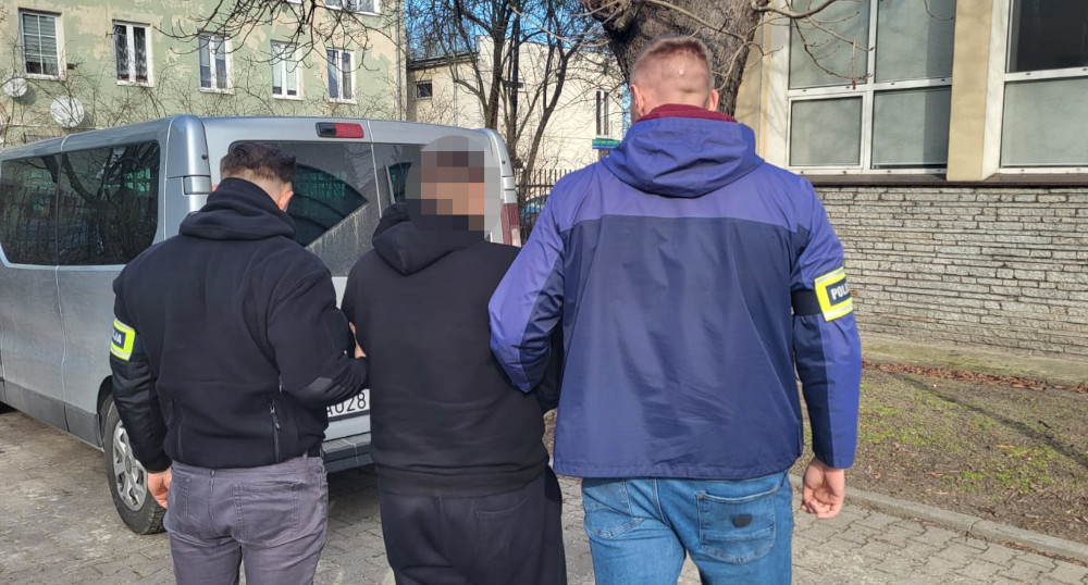 Trzech mężczyzn, w tym dwóch w odzieży policyjnej, prowadzi osobę podejrzaną w kierunku samochodu dostawczego.