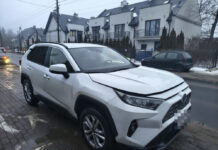 Biały SUV zaparkowany na chodniku w pobliżu nowoczesnych budynków mieszkalnych w deszczowy dzień.