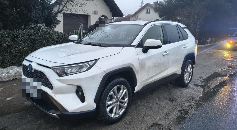 Biały SUV zaparkowany na poboczu drogi w otoczeniu domów jednorodzinnych.