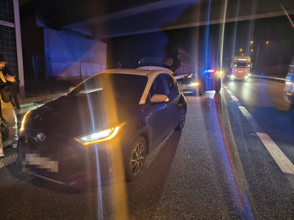 Samochód osobowy marki Toyota stoi na poboczu drogi, obok niego policyjny radiowóz oraz ciężarówka, w nocy.