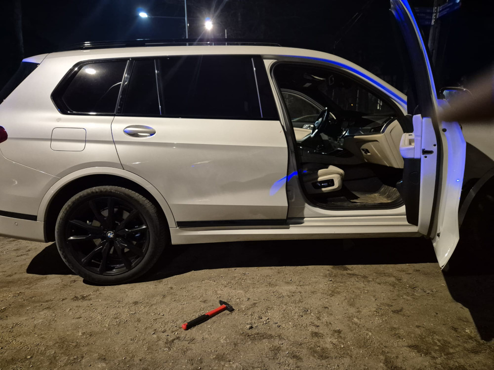 Biały SUV z otwartymi drzwiami, stojący na nieutwardzonej drodze, w otoczeniu nocnego oświetlenia.