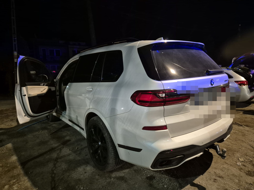 Biały SUV zaparkowany na ciemnej ulicy, z otwartymi drzwiami z przodu. W tle widać inne pojazdy.