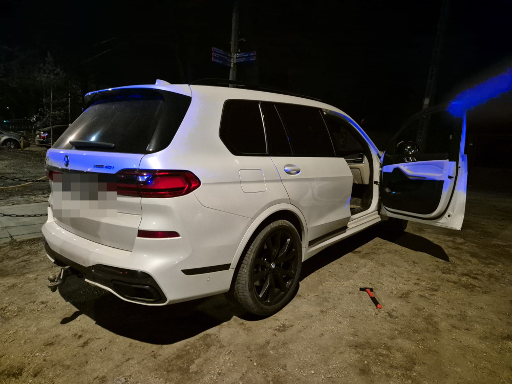 Biały SUV zaparkowany na nieoświetlonym terenie, z otwartymi drzwiami i widocznymi czarnymi felgami.