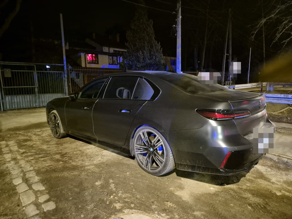 Czarny luksusowy samochód zaparkowany na ciemnej ulicy, w tle widoczne oświetlenie budynków.