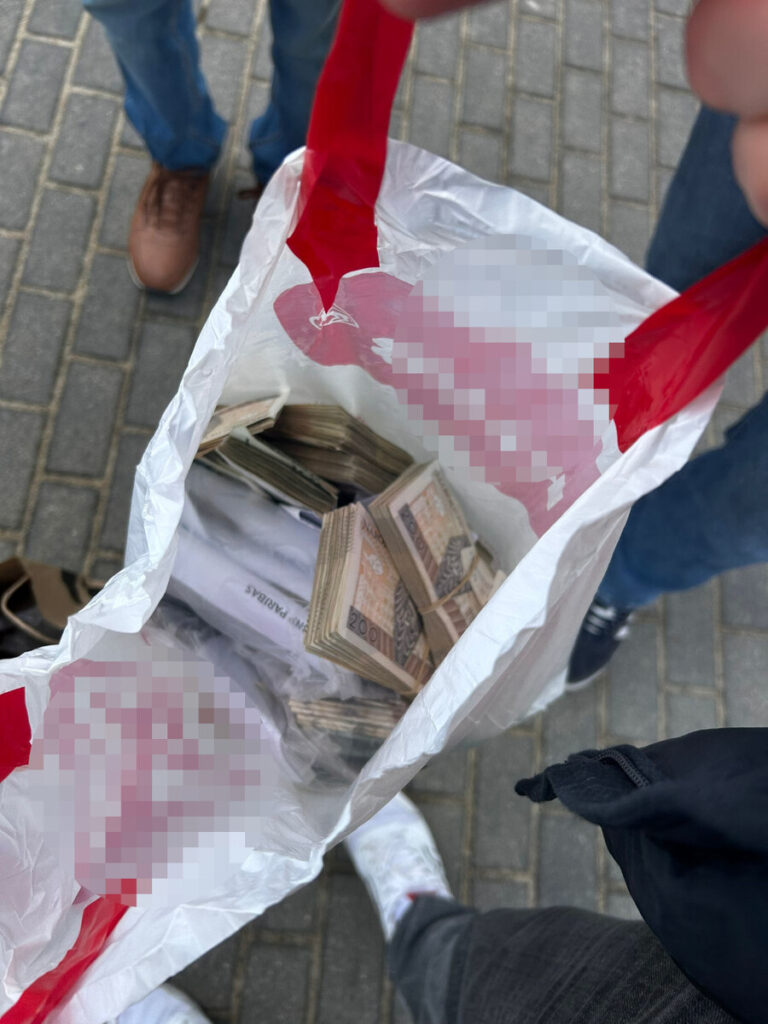 Torba na zakupy z czerwonymi uchwytami wypełniona banknotami, trzymana w ręce na chodniku.