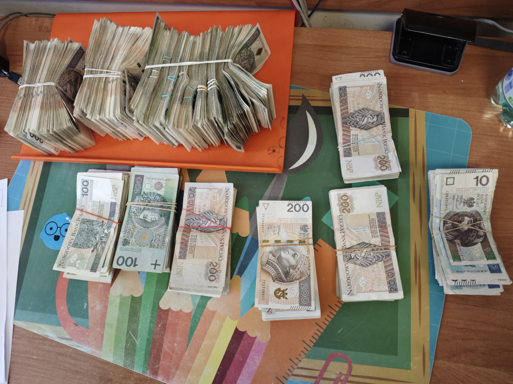 Stosy banknotów polskich na pomarańczowej tacy, ułożone według nominałów, na kolorowym tle biurowym.