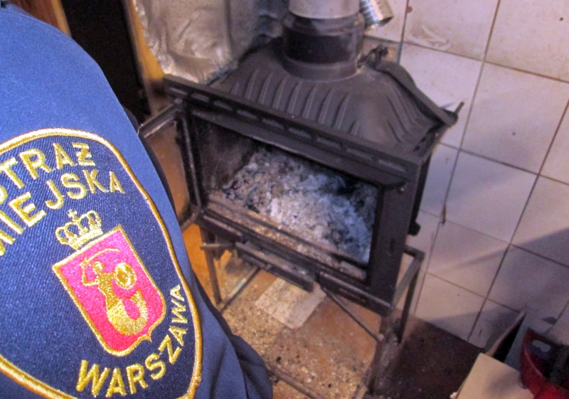 Mężczyzna w mundurze straży miejskiej stoi obok pieca z popiołem w kuchni.