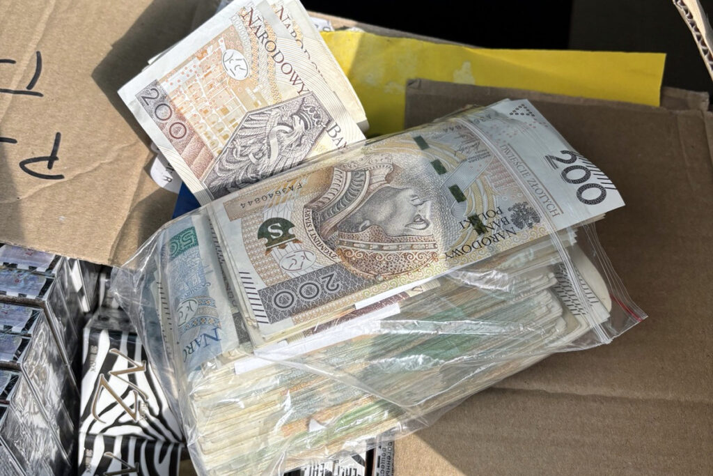 Pakunek z dużą ilością banknotów 200-złotowych i 50-złotowych leży na kartonie.