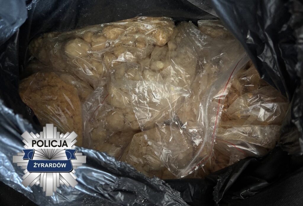 Torba z czarnego plastiku wypełniona przezroczystymi torebkami z substancją. W tle logo policji.