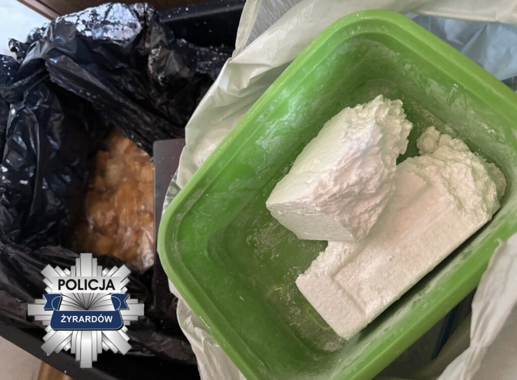 Biały proszek umieszczony w zielonym pojemniku, obok czarnych worków na śmieci w pomieszczeniu.