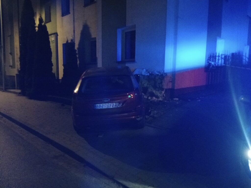 Czerwony samochód zaparkowany na chodniku obok budynku, oświetlony niebieskim światłem.