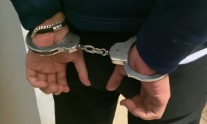 Mężczyzna w kajdankach stoi z rękami za plecami w zamkniętym pomieszczeniu.