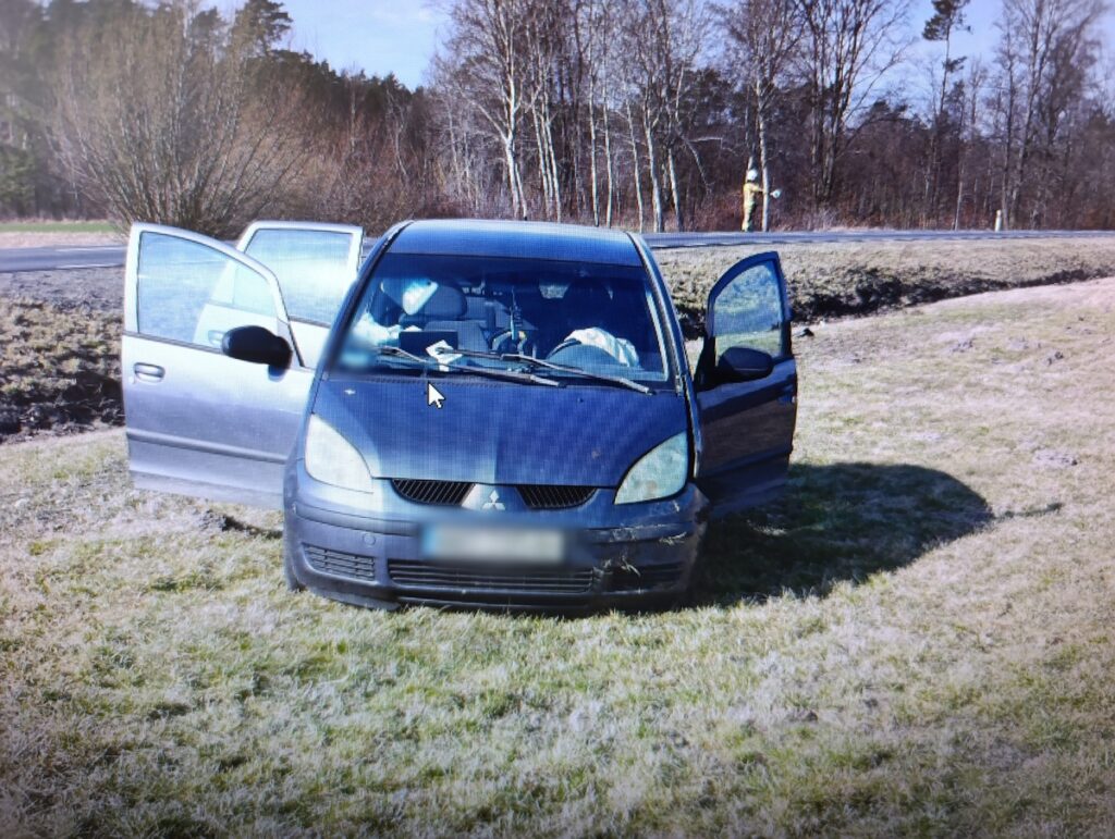 Czarny samochód osobowy z otwartymi drzwiami zaparkowany na poboczu drogi wśród drzew.