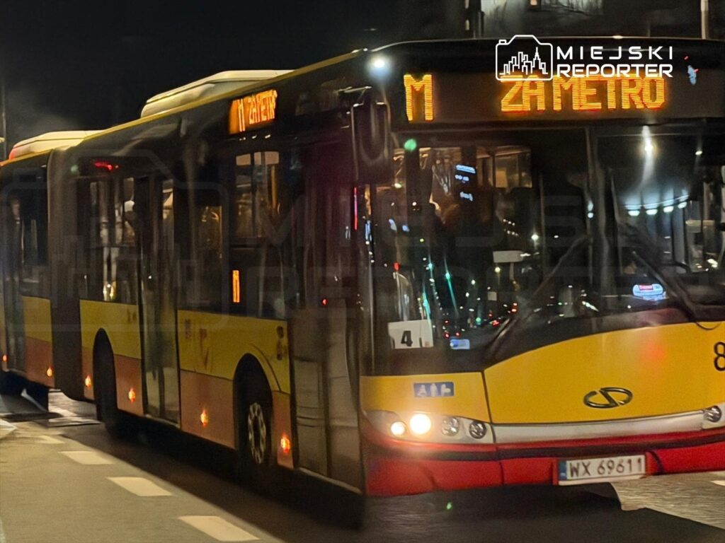 Autobus linii M z wyświetlaczem "ZAMETRO" zatrzymuje się na ulicy w nocy, oświetlony miejskim oświetleniem.