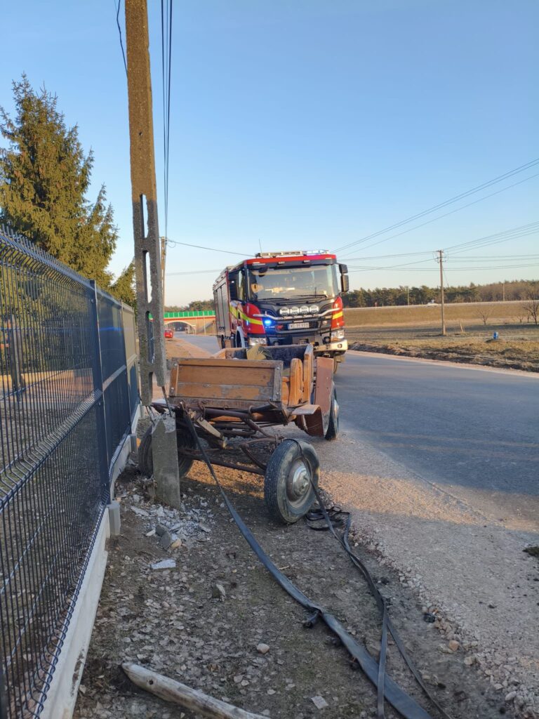 Strażacki wóz bojowy zatrzymany przy uszkodzonej przyczepie, obok której leżą fragmenty betonu i przewody.
