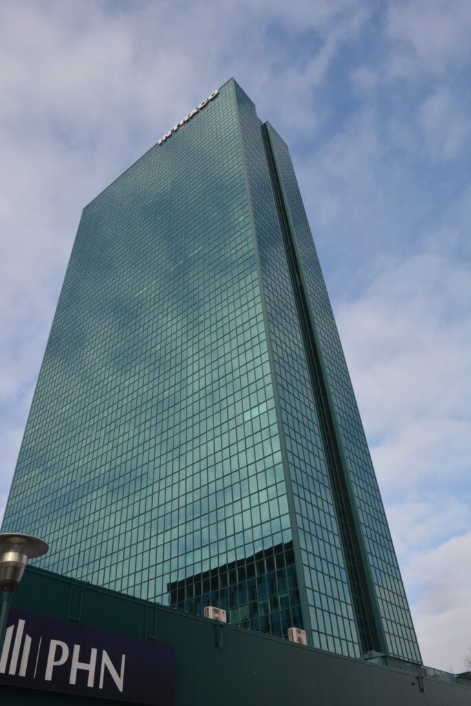 Nowoczesny biurowiec z przeszkloną fasadą, odbijający chmury na niebie, z logotypem PHN na dolnej części budynku.