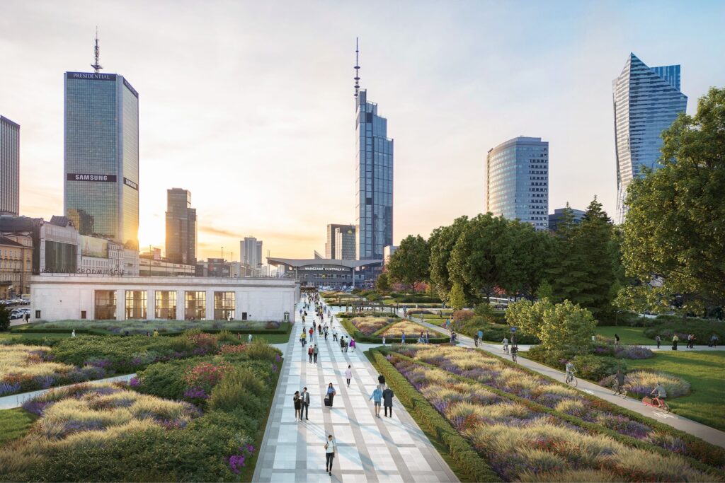 Grupa ludzi spaceruje po nowoczesnej promenadzie otoczonej kwiatami i drzewami w tle wieżowce.