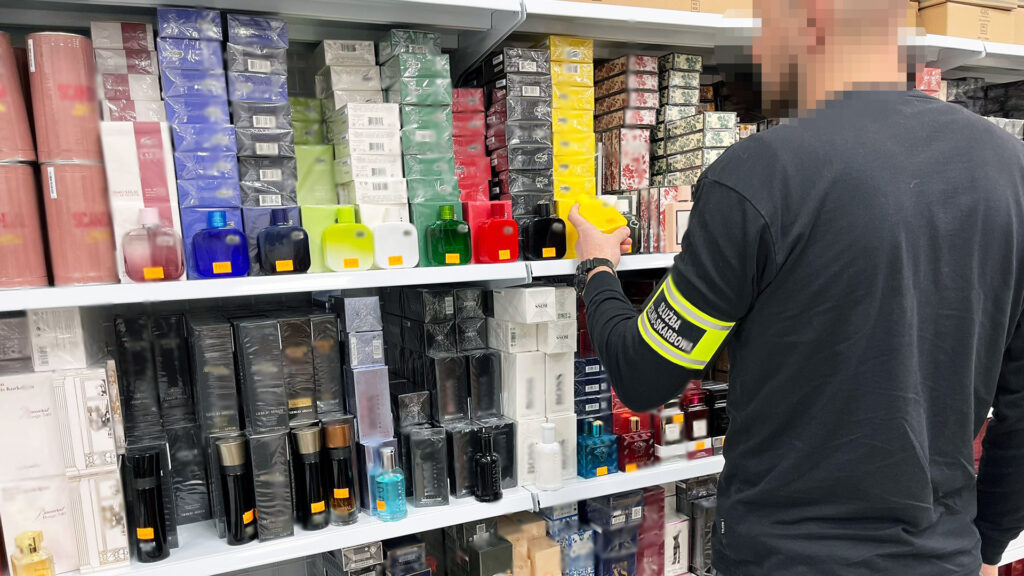 Mężczyzna w czarnej koszulce z żółtą opaską wybiera perfumy na półce w sklepie.