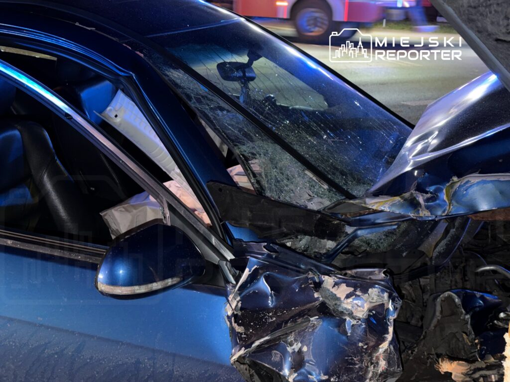 Zniszczony niebieski samochód osobowy z wybitymi szybami i uszkodzoną karoserią na drodze.