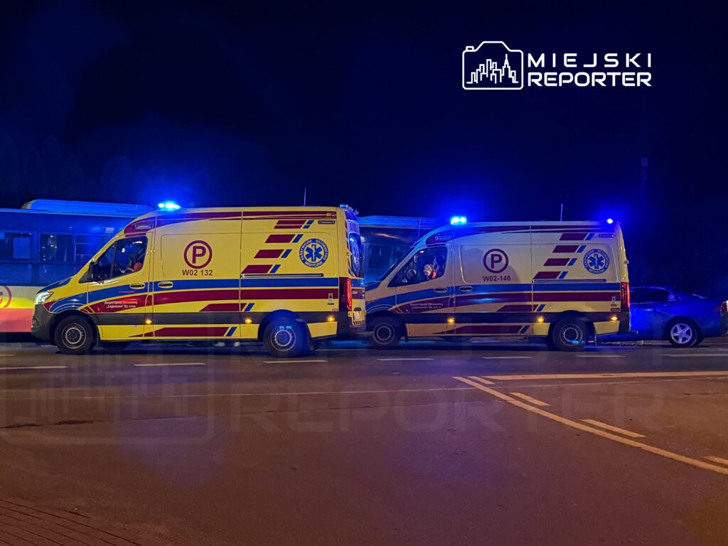 Dwa karetki pogotowia z włączonymi sygnalizatorami świetlnymi zatrzymane na drodze w nocy.