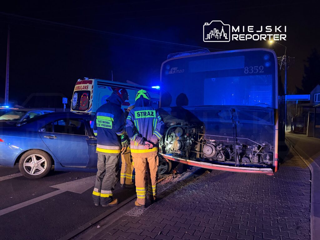 Strażacy w specjalistycznych ubraniach omawiają sytuację przy uszkodzonym autobusie na nocnej ulicy.