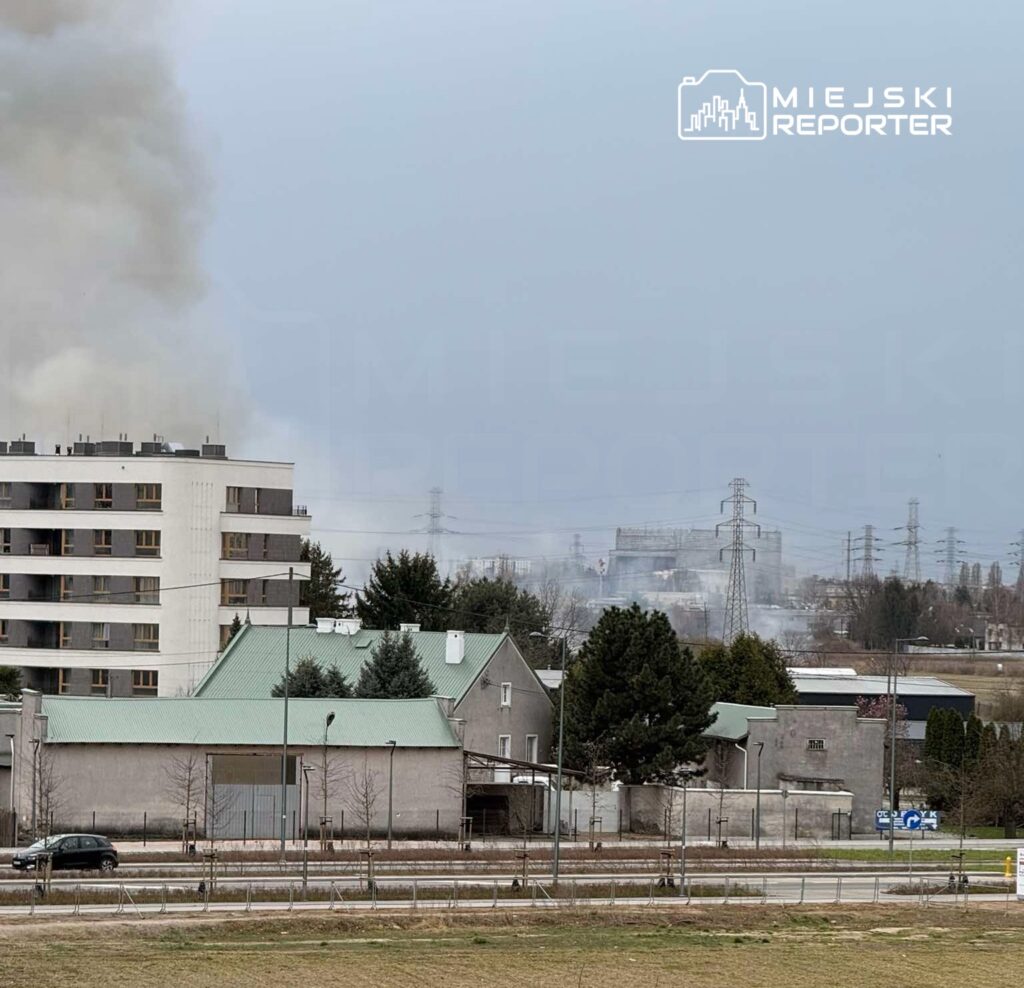 Gęsty dym unoszący się nad osiedlem mieszkaniowym w tle z przemysłowymi budynkami i liniami energetycznymi.