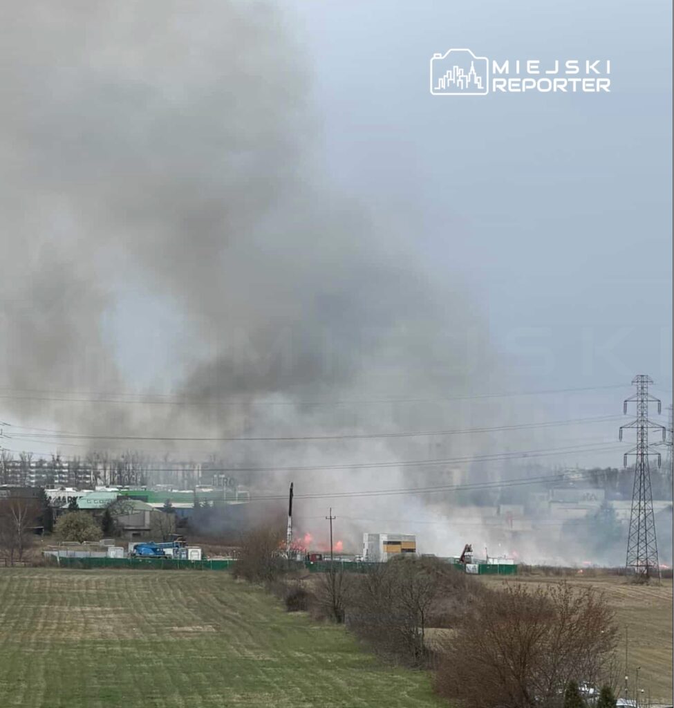 Gęsty dym unoszący się nad terenem przemysłowym, w tle widoczne maszyny i zieleń.
